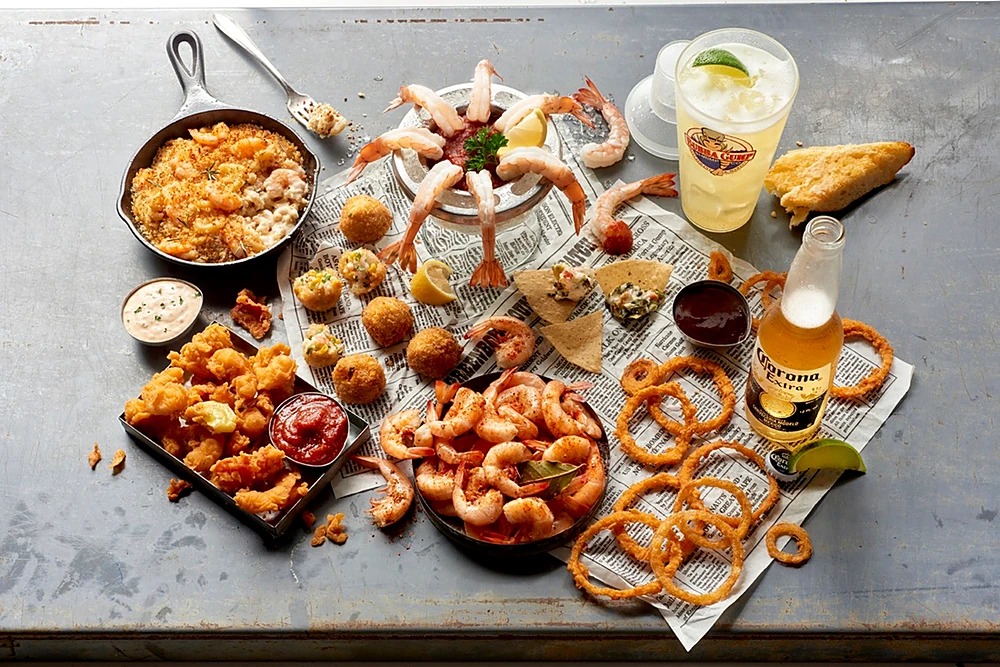 A shared spread of Bubba Gump favourites — shrimp, onion rings and a cold drink on newspaper